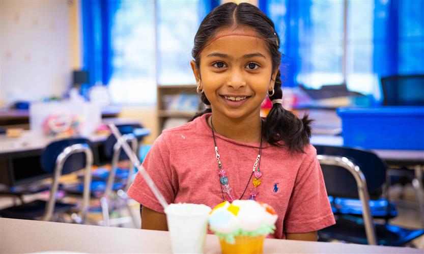 A girl wearing a pink shirt smiles while decorating a cupcake